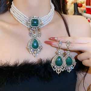 Close-up of vintage pearl necklace and earrings set with emerald green teardrop stones.