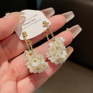 Vue détaillée de boucles d'oreilles fleurs blanches avec chaînes dorées en argent.