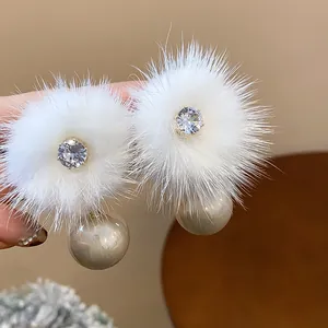 Primo piano di orecchini di peluche bianchi con zircone e grandi perle champagne.