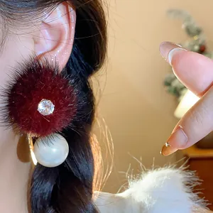 Dettaglio di un elegante orecchino a pompon in pelliccia bordeaux con zircone e perla