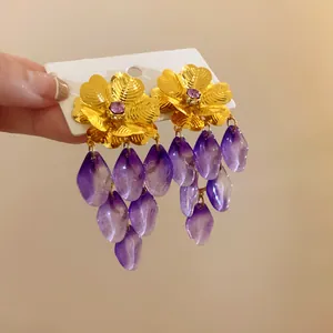 Dettaglio squisito di orecchini a fiore vintage in oro con petali viola pendenti