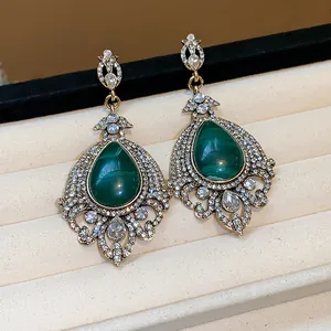Detail view of vintage-style teardrop earrings featuring green stones and sparkling rhinestones.