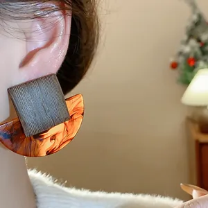 Close-up of square resin stud earrings with wood texture and amber semi-circle detail.