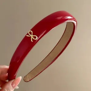 Detailed view of a red glossy headband featuring a delicate golden bow ornament.