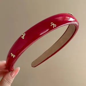 Close-up of a glossy red padded headband featuring delicate golden bow embellishments.