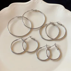 Detailed view of minimalist silver hoop earrings in four various sizes on a white plate