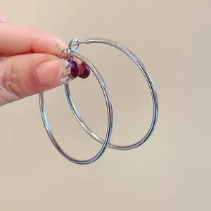 Minimalist large silver hoop earrings for women shown held against a beige background