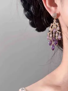 Élégantes boucles d'oreilles chandelier dorées 18 carats avec zircons violets sur modèle