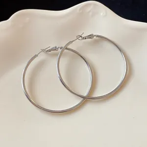 Detail view of large minimalist silver hoop earrings resting on a white decorative plate.