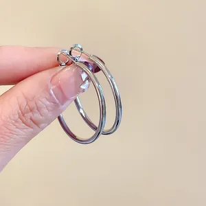 Macro view of minimalist silver hoop earrings held in hand showing high polish finish