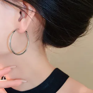 A detailed close-up shot showing a large minimalist silver hoop earring worn on the ear.