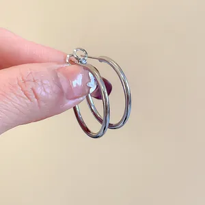 Detailed view of minimalist polished silver round hoop earrings held by a hand.