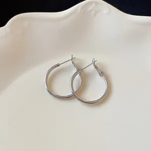 Close-up of minimalist silver hoop earrings on a decorative white scalloped plate