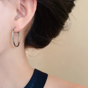 Close-up of a minimalist silver hoop earring worn on an ear, showing sleek texture.