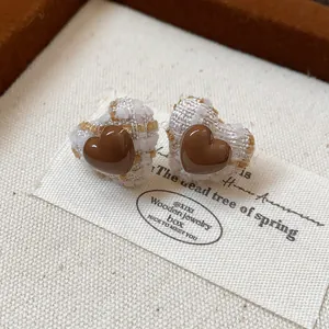 Detailansicht der herzförmigen Ohrstecker mit braunem Harz und Tweed-Stofftextur