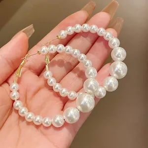 Detailed macro view of elegant vintage style graduated pearl hoop earrings held in hand.