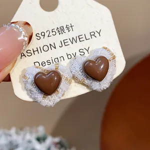 Nahaufnahme von herzförmigen Harzohrringen mit weißem Tweed-Rand auf einer Displaykarte.