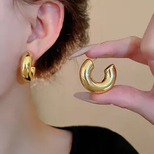 Detailed macro view of a chunky golden metal C-shaped hoop earring held by hand