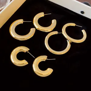 Detailed close-up view of minimalist gold-plated C-shaped hoop earrings on black velvet background