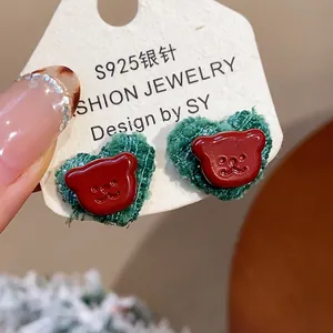 Nahaufnahme von Herz-Ohrringen mit rotem Harz-Bären und grüner Stofftextur