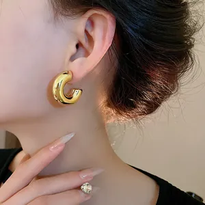 Close-up view of minimalist gold C-shaped chunky stud earrings worn on a female ear model