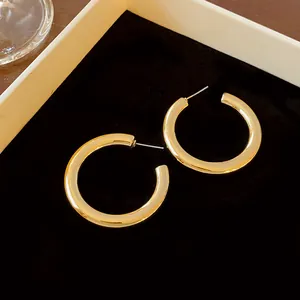 Detailed close-up view of chunky gold C-shaped hoop earrings on a black velvet background