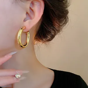 Close-up of model wearing thick gold C-shaped hoop earrings with a premium glossy finish.