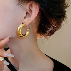 Detailed close-up of a minimalist chunky gold C-shaped hoop earring worn by a female model