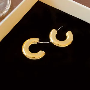 Close-up detail of minimalist chunky C-shaped gold hoop earrings on black velvet