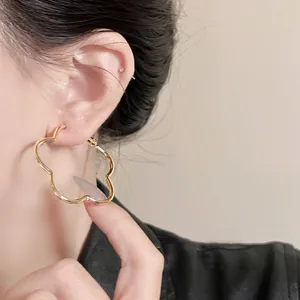 Elegant gold flower-shaped hoop earring with a wavy scalloped design worn by a model.