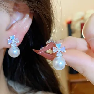 Close-up detail of silver pin earrings with zircon flower and white pearl drop