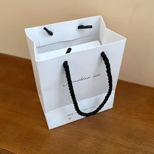 Minimalist white jewelry gift bag featuring black rope handles and elegant cursive text
