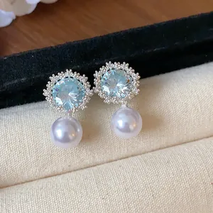 Close-up detail of elegant zircon flower stud earrings with a dangling round white pearl