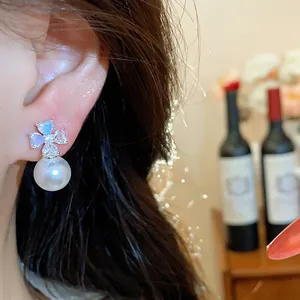 Detailed view of elegant zircon flower earrings with white pearl drop on model