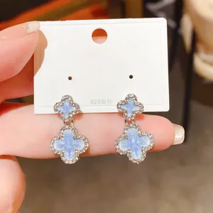 Close-up shot of blue four-leaf clover drop earrings featuring sparkling zircon border details