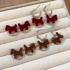 Close-up of retro flocked rocking horse earrings with zircon accents on fabric display.