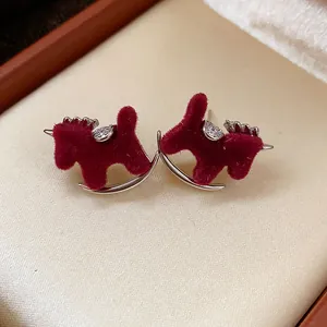 Close-up of red flocked rocking horse stud earrings with zircon accents on beige background