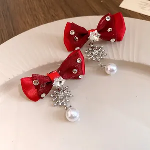 Detailed macro shot of red fabric bow earrings with snowflake charms and white pearls