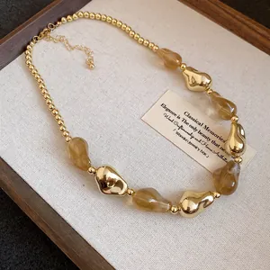 Primo piano di una collana in stile retrò con perle acriliche irregolari oro e ambra.
