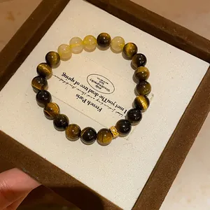 Close-up view of tiger eye stone bead bracelet with gold floral charm in a luxury gift box