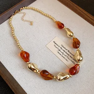 Primo piano di una collana stile retrò con perle in acrilico ambra e oro geometrico