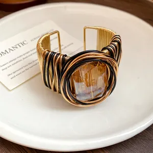 Dettaglio ravvicinato del bracciale rigido in filo intrecciato oro e nero con vetro ambra