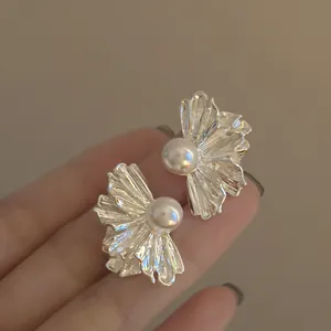 Dettaglio macro di orecchini a fiore pieghettati in argento con un'elegante perla