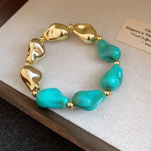 Dettaglio di un bracciale con perle acriliche irregolari oro e turchese su sfondo neutro