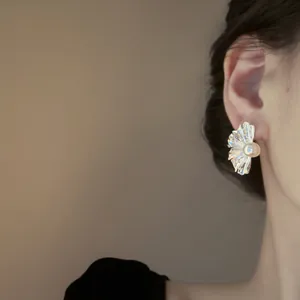 Eleganti orecchini francesi a forma di fiore stropicciato con perla indossati all'orecchio.