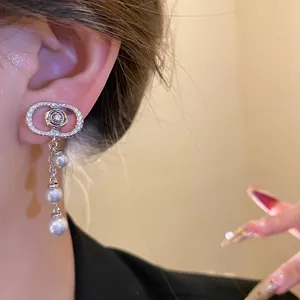 Close-up of 18k gold-plated zircon oval earrings with pearl tassels worn on an ear.