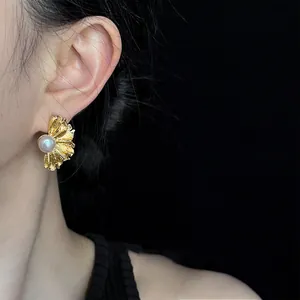 Primo piano di un elegante orecchino a fiore plissettato dorato con perla sull'orecchio