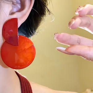 Close-up view of retro asymmetrical red resin round drop earrings worn on a model's ear
