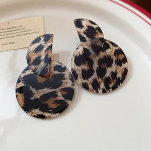 Close-up of retro leopard print asymmetric round drop earrings on a white ceramic plate