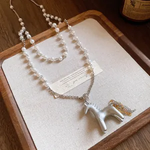 Collier élégant avec pendentif cheval argenté mat, perles blanches et glands de chaîne.